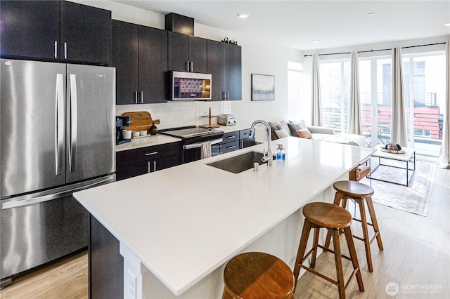 kitchen with tasteful backsplash, sink, a kitchen breakfast bar, a kitchen island with sink, and stainless steel appliances