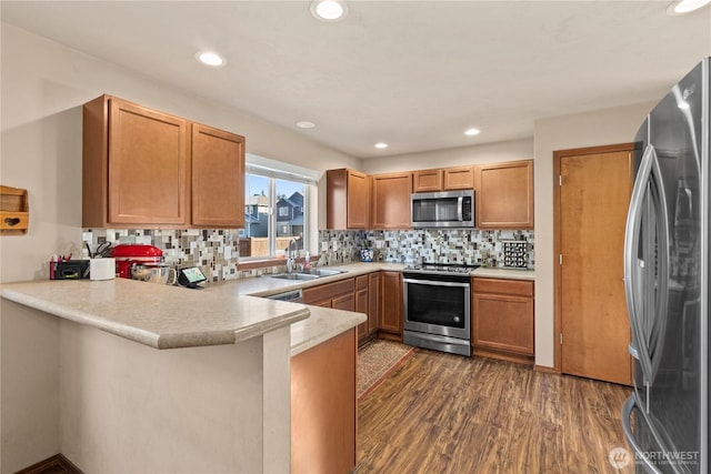 kitchen with sink, backsplash, dark hardwood / wood-style flooring, kitchen peninsula, and stainless steel appliances