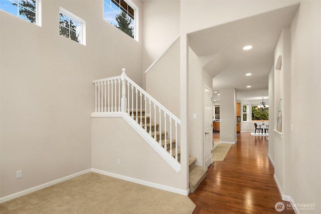 stairs with a towering ceiling, wood-type flooring, and a notable chandelier