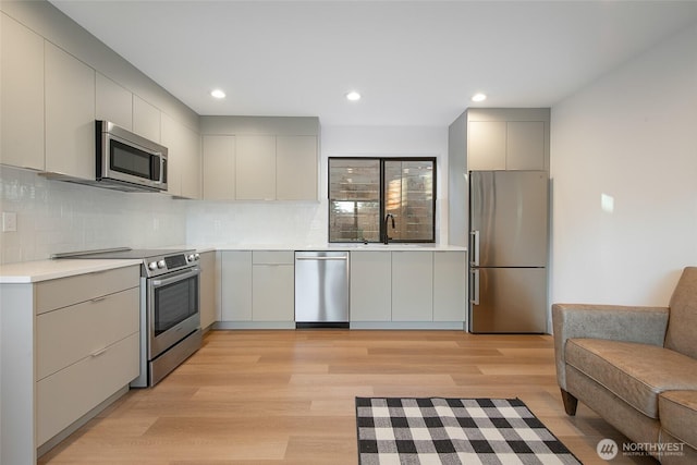 kitchen with sink, appliances with stainless steel finishes, gray cabinetry, backsplash, and light hardwood / wood-style floors