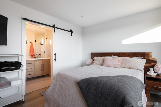 bedroom featuring sink, connected bathroom, hardwood / wood-style flooring, and a barn door