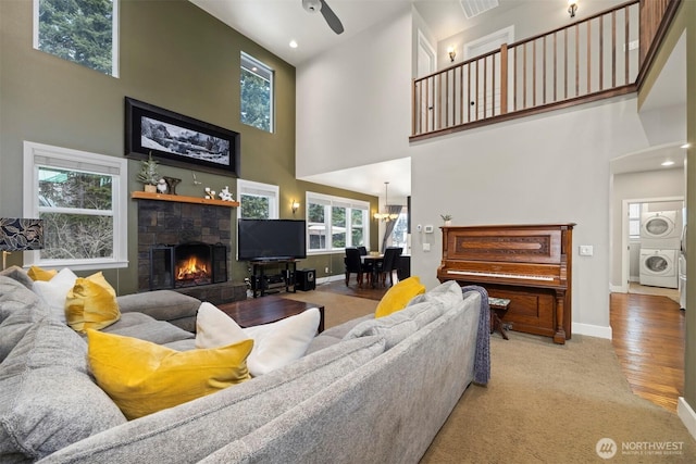 living room featuring a stone fireplace, a towering ceiling, stacked washer / dryer, ceiling fan, and light hardwood / wood-style floors