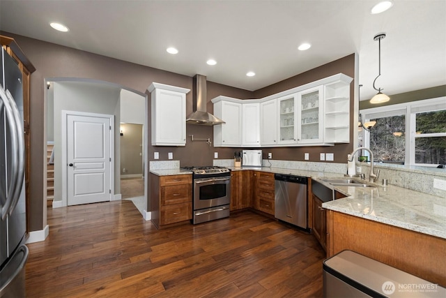 kitchen featuring wall chimney range hood, stainless steel appliances, light stone countertops, white cabinets, and decorative light fixtures