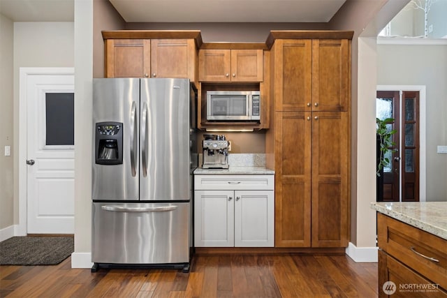 kitchen with appliances with stainless steel finishes, dark wood-type flooring, and light stone counters