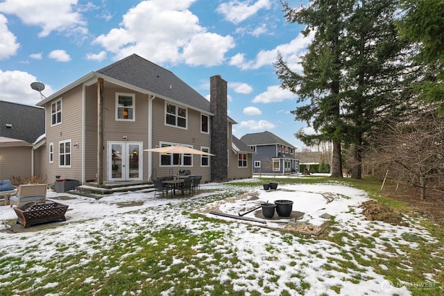 snow covered back of property with french doors and a fire pit