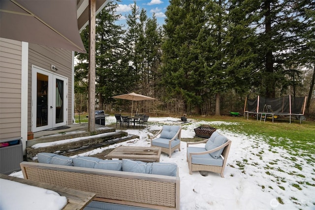 snow covered patio with french doors, grilling area, an outdoor living space, and a trampoline