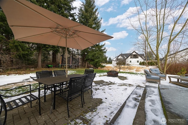 snow covered patio featuring a trampoline and an outdoor fire pit