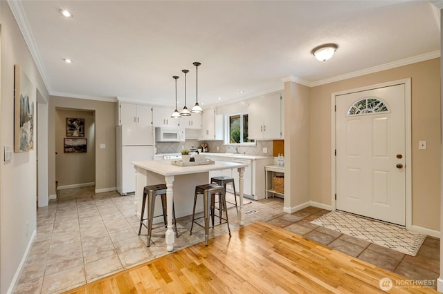 kitchen with white appliances, white cabinetry, hanging light fixtures, a center island, and decorative backsplash