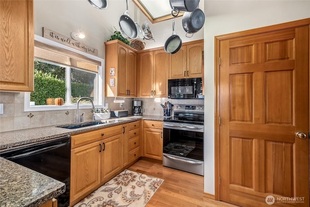 kitchen featuring light wood-type flooring, black appliances, sink, tasteful backsplash, and dark stone countertops