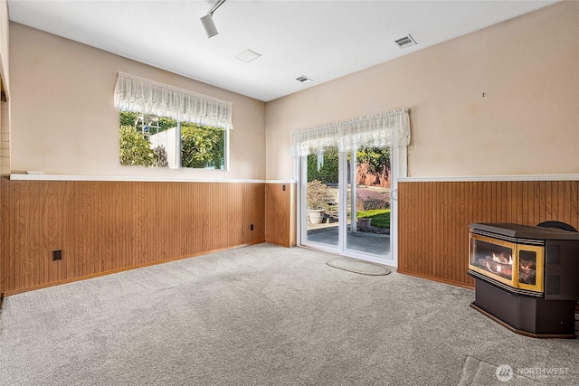 unfurnished living room with wood walls, a wood stove, light colored carpet, and track lighting