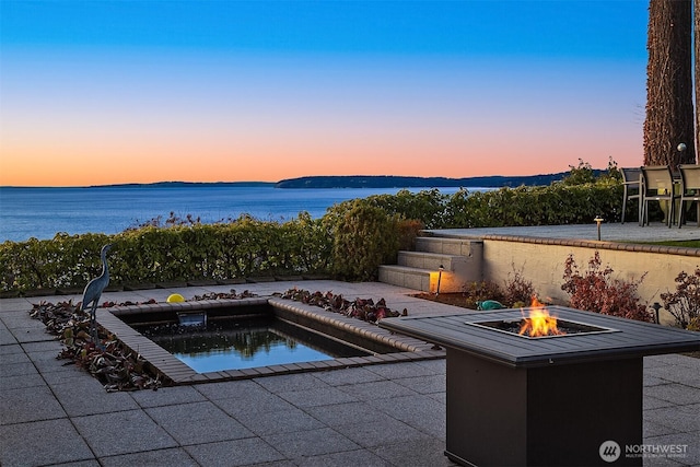 pool at dusk featuring a patio area, a water view, and an outdoor fire pit