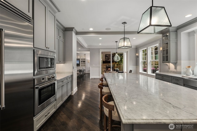 kitchen featuring gray cabinetry, built in appliances, hanging light fixtures, ornamental molding, and a kitchen breakfast bar