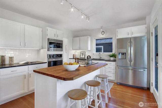 kitchen featuring white cabinets, a center island, appliances with stainless steel finishes, and wooden counters