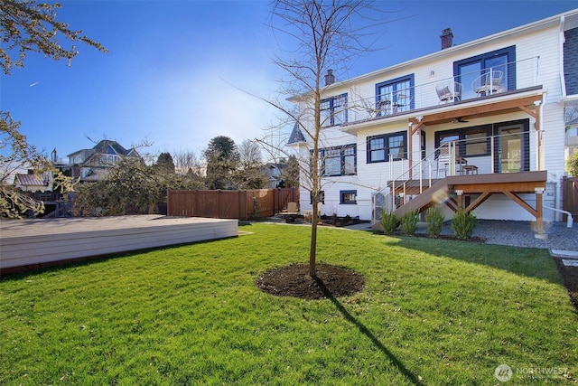 rear view of property featuring a lawn, a deck, ceiling fan, and a balcony