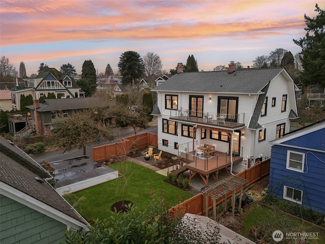 back house at dusk with a balcony and a lawn