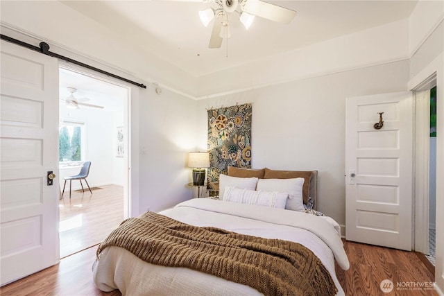 bedroom featuring hardwood / wood-style flooring, a barn door, and ceiling fan