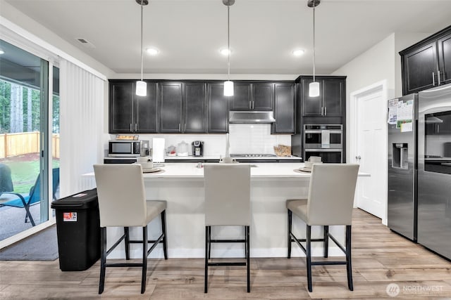 kitchen featuring under cabinet range hood, appliances with stainless steel finishes, light countertops, and decorative light fixtures