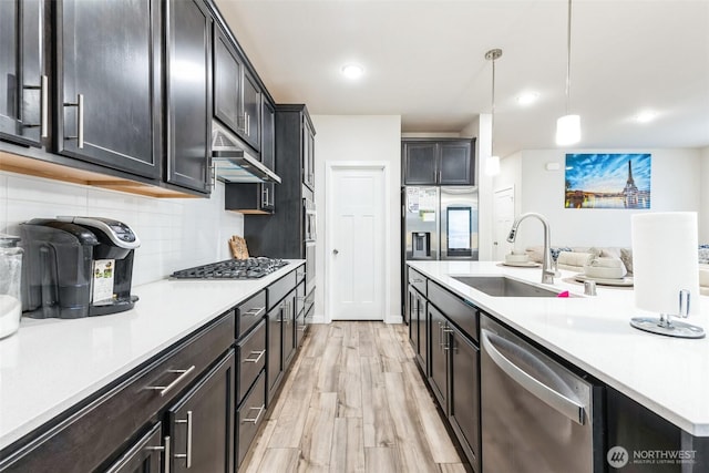 kitchen with under cabinet range hood, stainless steel appliances, a sink, hanging light fixtures, and light countertops