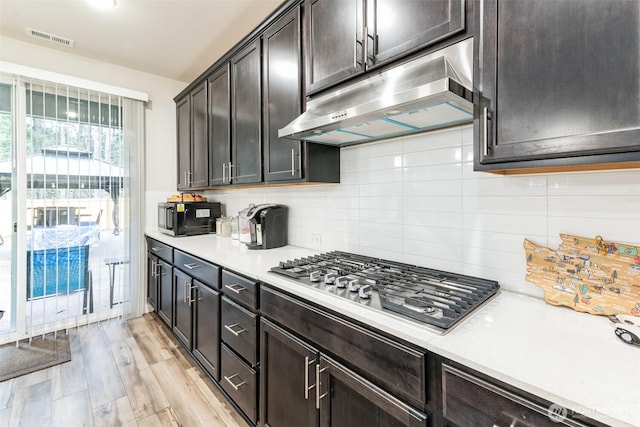 kitchen with dark brown cabinetry, under cabinet range hood, light countertops, light wood finished floors, and stainless steel gas stovetop