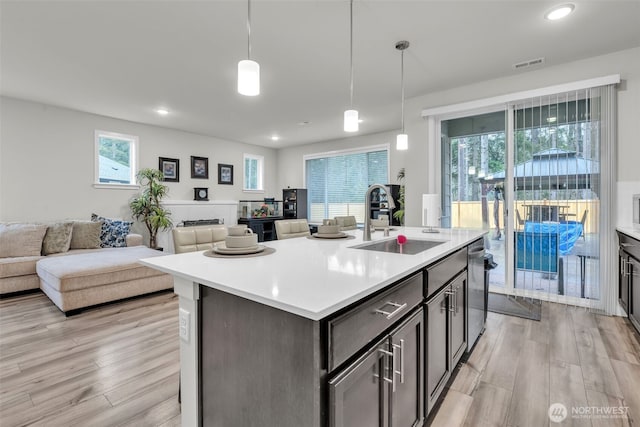 kitchen with visible vents, light countertops, hanging light fixtures, open floor plan, and a sink