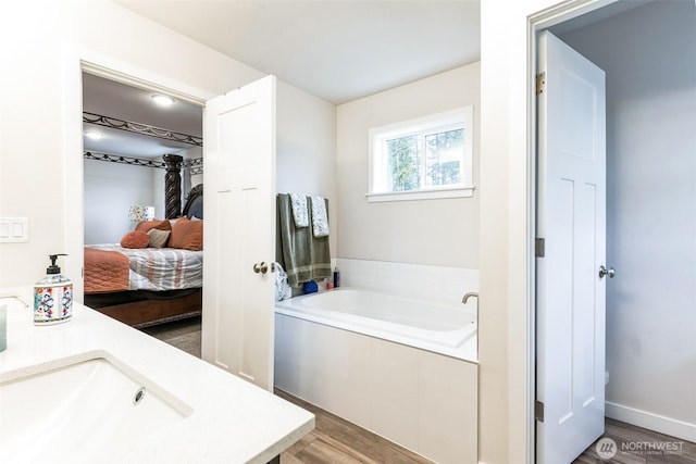 ensuite bathroom with a sink, wood finished floors, ensuite bath, and a bath