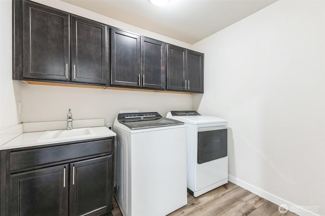 laundry room with cabinet space, baseboards, light wood-type flooring, washing machine and dryer, and a sink