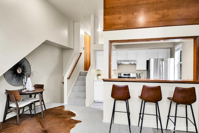 kitchen with stainless steel appliances, light colored carpet, white cabinets, and a kitchen breakfast bar