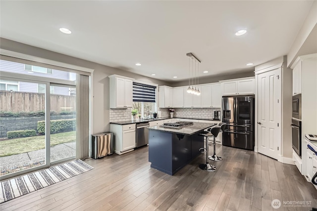 kitchen with a breakfast bar, a kitchen island, white cabinets, appliances with stainless steel finishes, and decorative light fixtures