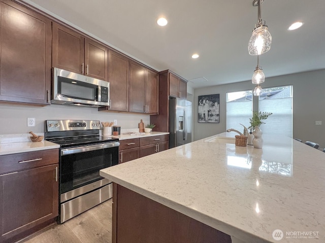 kitchen with light stone countertops, stainless steel appliances, dark brown cabinets, pendant lighting, and a sink