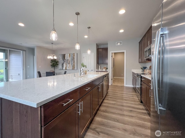 kitchen with stainless steel appliances, a spacious island, dark brown cabinetry, a sink, and light wood-type flooring