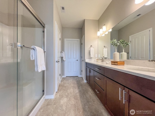 bathroom featuring a sink, a shower stall, baseboards, and double vanity