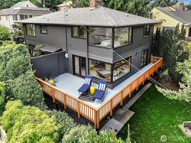 rear view of property featuring a shingled roof, a chimney, and a deck