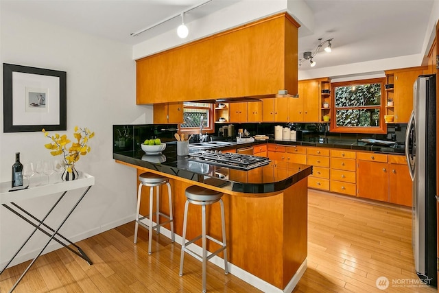 kitchen with light wood-style flooring, a peninsula, a kitchen breakfast bar, appliances with stainless steel finishes, and open shelves