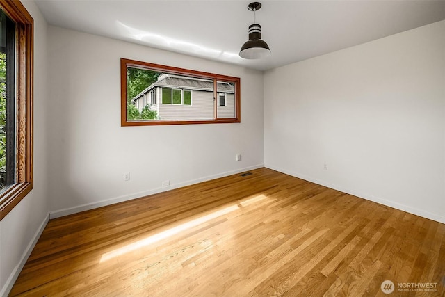 empty room featuring wood finished floors, visible vents, and baseboards