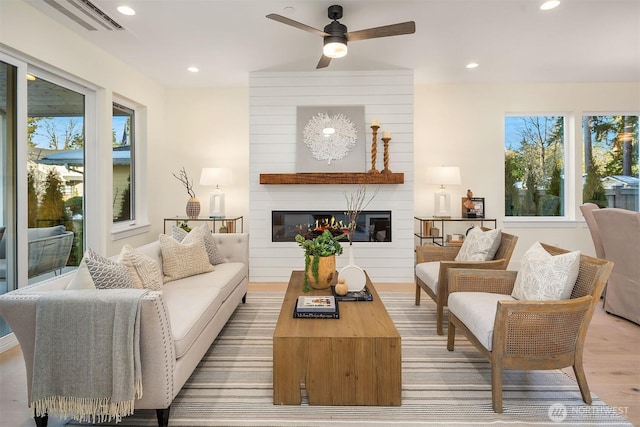 interior space featuring ceiling fan, a large fireplace, and light wood-type flooring