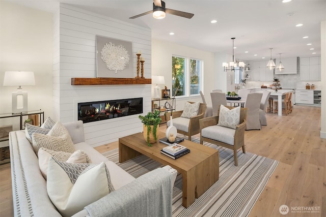 living room featuring ceiling fan with notable chandelier and light hardwood / wood-style flooring