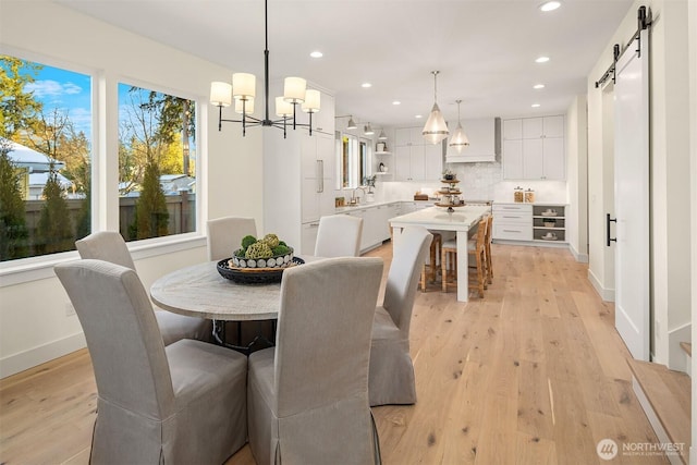 dining room featuring a barn door, a chandelier, and light wood-type flooring