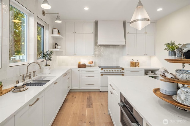 kitchen featuring pendant lighting, high end white range oven, sink, white cabinets, and wall chimney exhaust hood