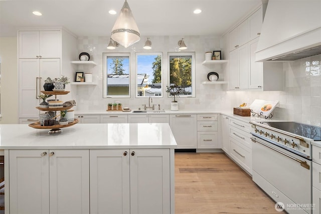 kitchen featuring pendant lighting, sink, high end white range, white cabinetry, and custom range hood