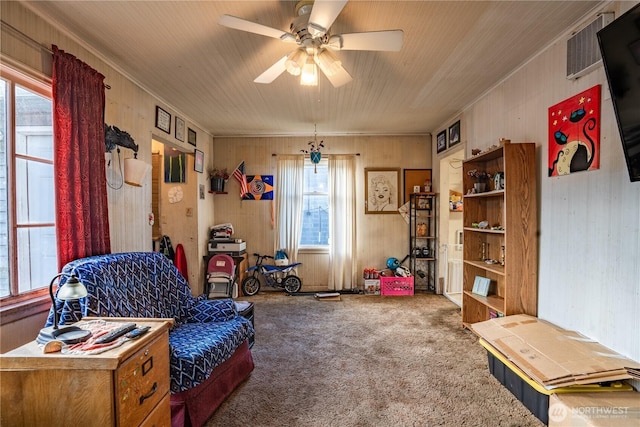 living area with carpet floors, ceiling fan, wood walls, and ornamental molding