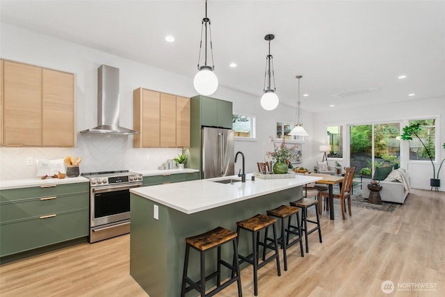 kitchen featuring appliances with stainless steel finishes, light brown cabinetry, light countertops, wall chimney exhaust hood, and pendant lighting