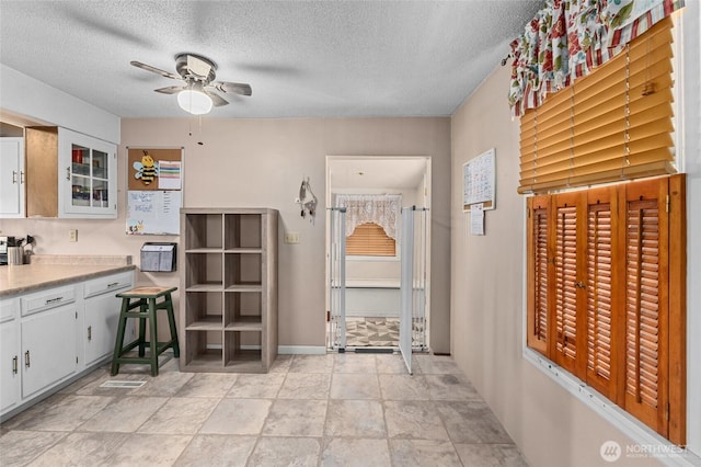 kitchen with white cabinetry, ceiling fan, and a textured ceiling