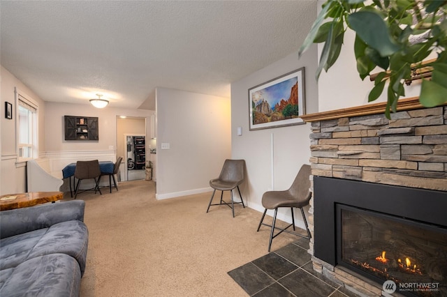 carpeted living room featuring a stone fireplace and a textured ceiling