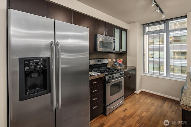 kitchen with hardwood / wood-style flooring, rail lighting, dark brown cabinets, stainless steel appliances, and dark stone counters