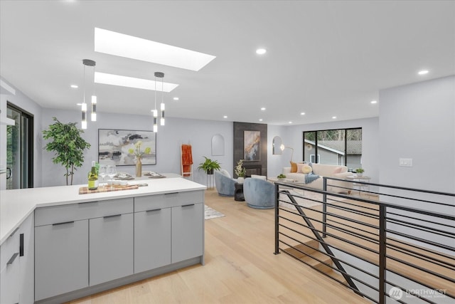 kitchen featuring gray cabinetry, pendant lighting, a skylight, and light hardwood / wood-style flooring