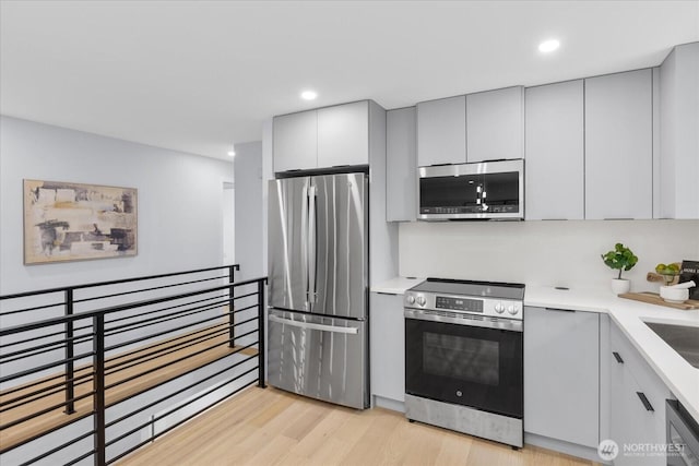 kitchen with gray cabinets, light hardwood / wood-style floors, stainless steel appliances, and sink