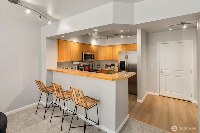 kitchen featuring appliances with stainless steel finishes, a breakfast bar, light wood-type flooring, and kitchen peninsula