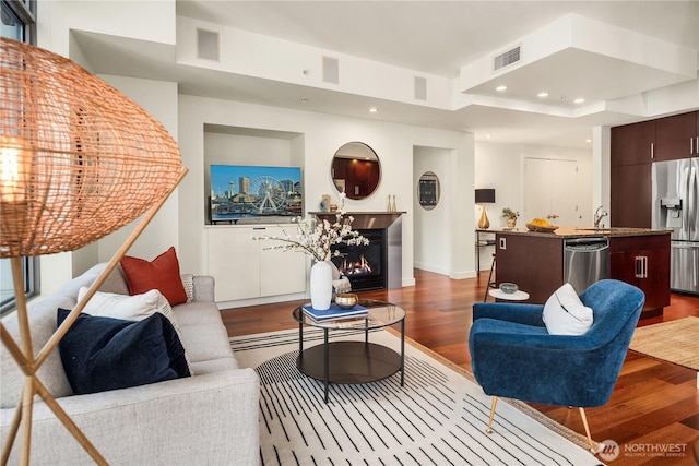 living room with dark hardwood / wood-style flooring, sink, and a tray ceiling