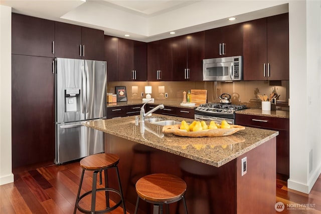 kitchen with appliances with stainless steel finishes, dark hardwood / wood-style floors, sink, a kitchen breakfast bar, and a kitchen island with sink