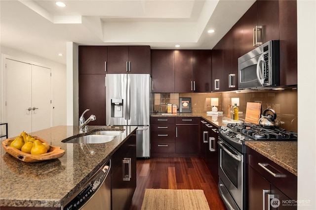 kitchen featuring sink, dark stone countertops, appliances with stainless steel finishes, dark hardwood / wood-style flooring, and decorative backsplash